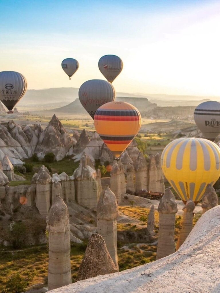 Scenic view of hot air balloons floating over Cappadocia's unique landscape during sunrise.