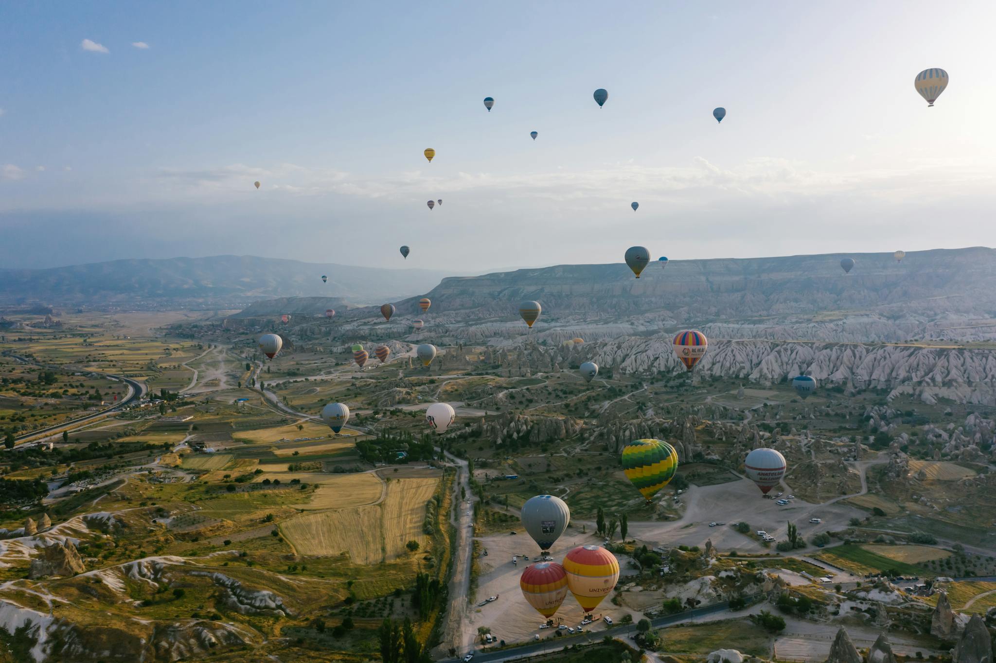 Captivating aerial view of vibrant hot air balloons floating over Cappadocia's unique rock formations and valleys.